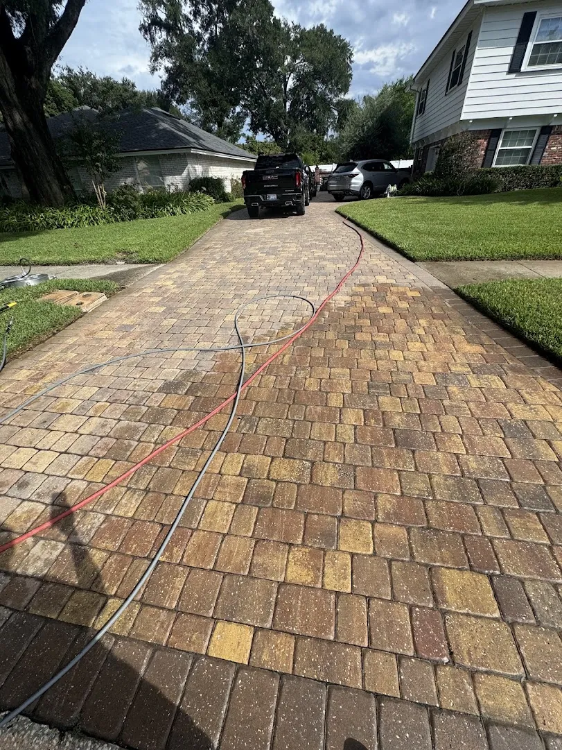Paver driveway being cleaned and sealed, hose running down the drive