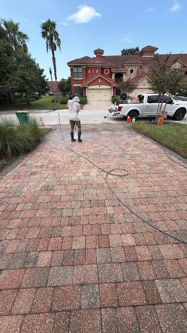 Technician pressure washing a paver driveway in front of a two-story Jacksonville home