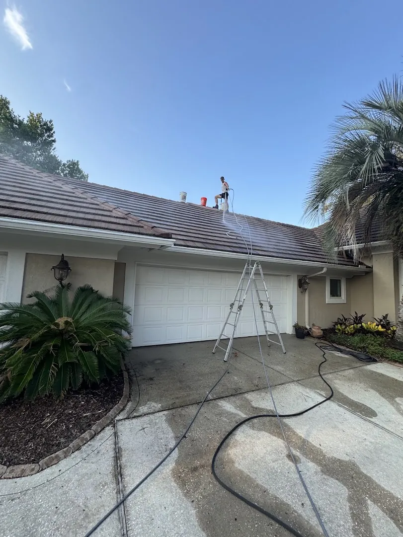 Technician on a ladder soft-washing a tile roof to remove black streaks